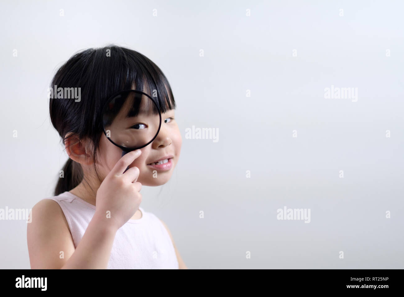 Little girl child looking through a magnifying glass on white background Stock Photo