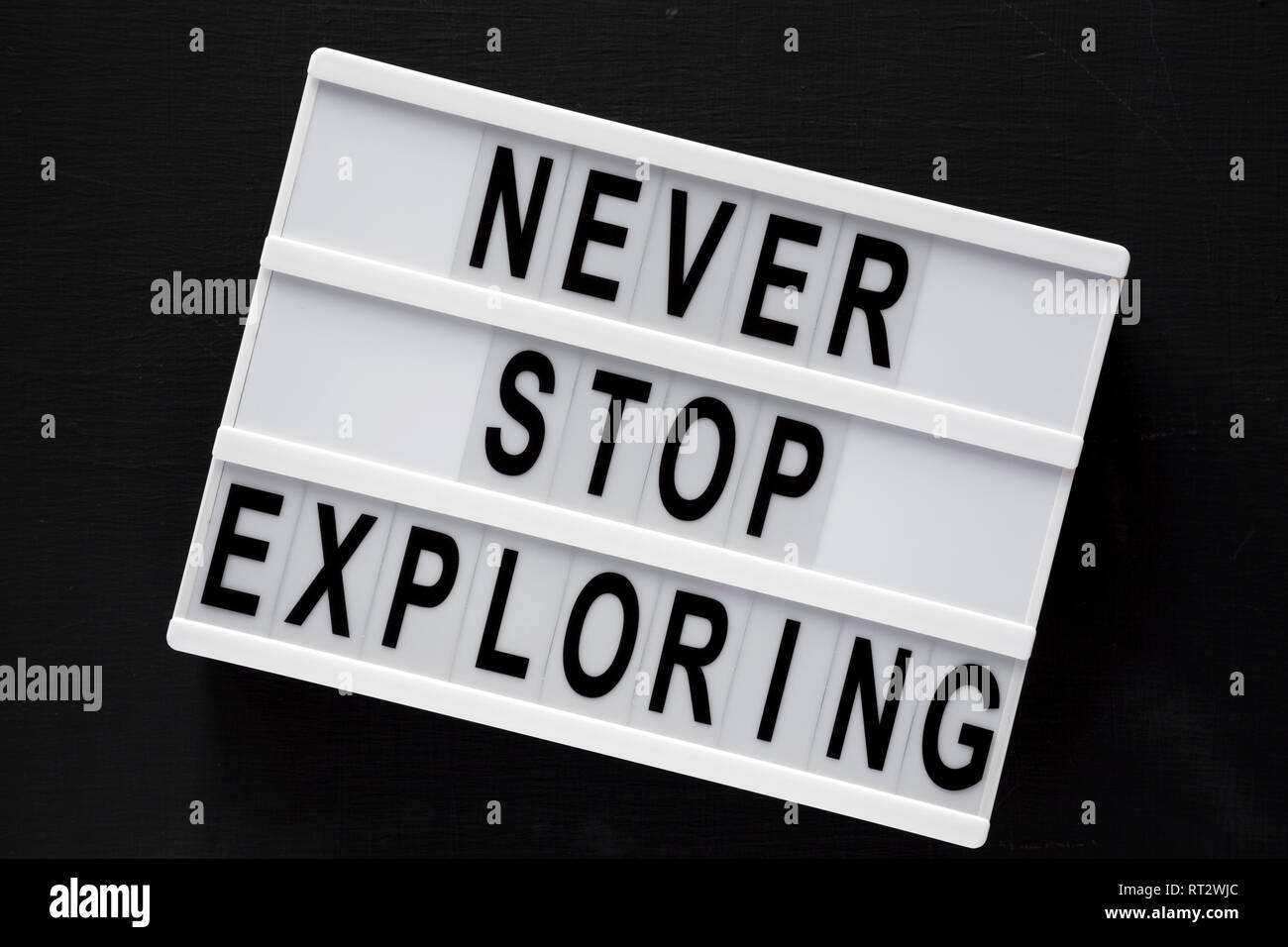 Lightbox with text 'Never stop exploring' over black background, top view. Overhead, flat lay, from above. Close-up. Stock Photo