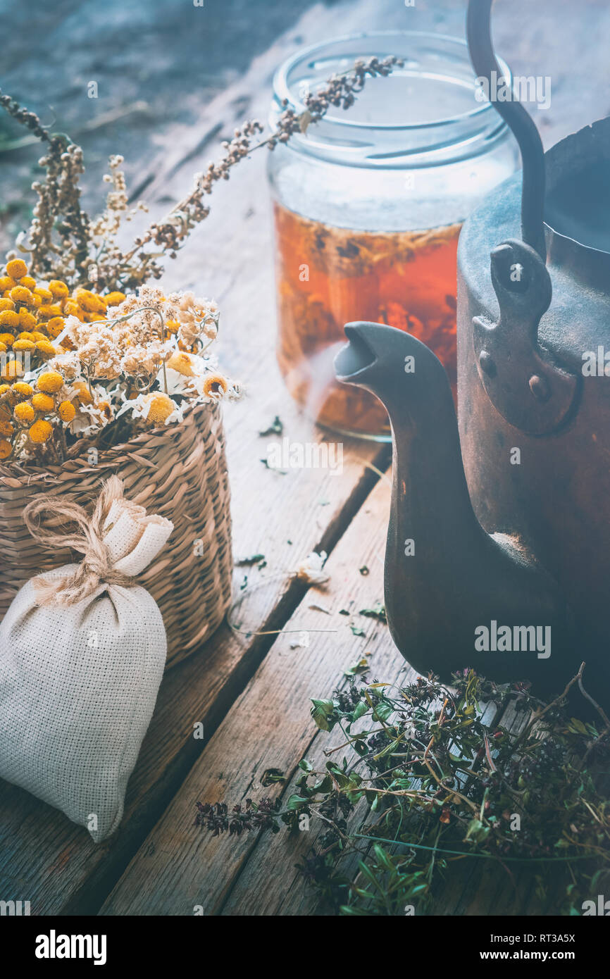 Healing herbs in basket, vintage tea kettle and jar of healthy tea. Herbal medicine. Retro toned