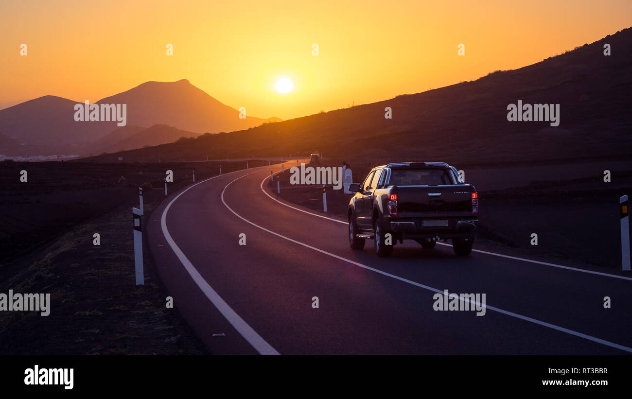 Car on a winding road driving towards sunset. Lanzarote Stock Photo