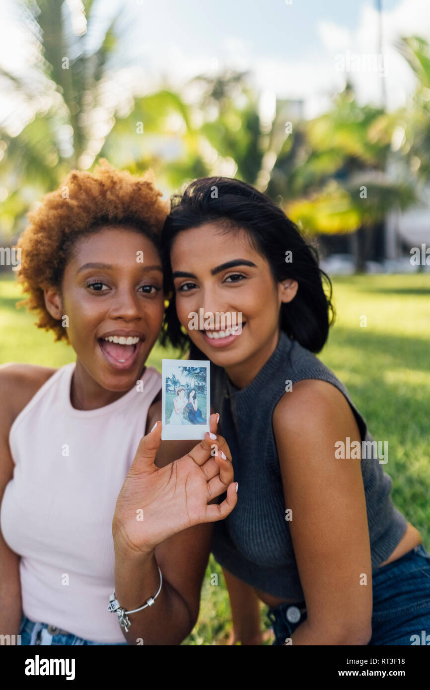 Two happy female friends showing an instant photo in a park Stock Photo