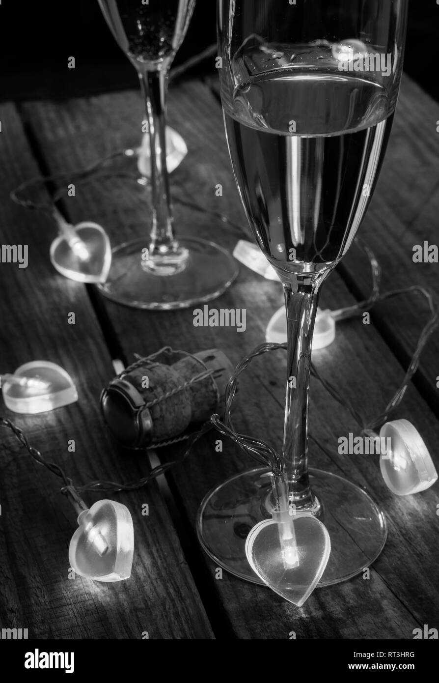 Two champagne glasses with love heart shaped fairy lights around on a wooden table Stock Photo