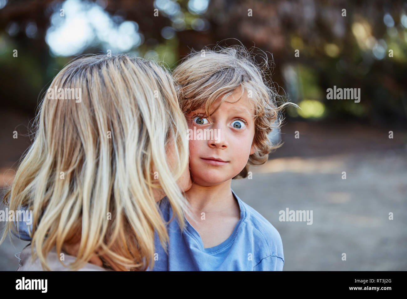 Portrait of wide-eyed boy being kissed by his mother Stock Photo