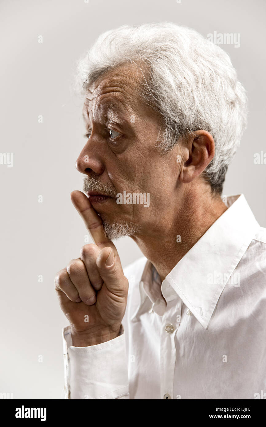 Serious senior frightened male keeps fore finger on lips, tries to keep conspiracy, says: Shh, make silence please. Isolated shot of man shows silence gesture Stock Photo