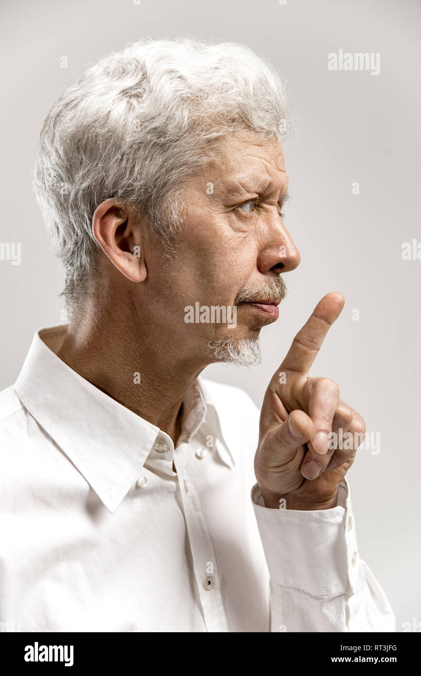 Serious senior frightened male keeps fore finger on lips, tries to keep conspiracy, says: Shh, make silence please. Isolated shot of man shows silence gesture Stock Photo