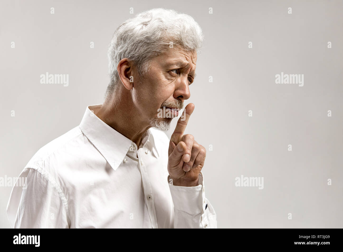 Serious senior frightened male keeps fore finger on lips, tries to keep conspiracy, says: Shh, make silence please. Isolated shot of man shows silence gesture Stock Photo