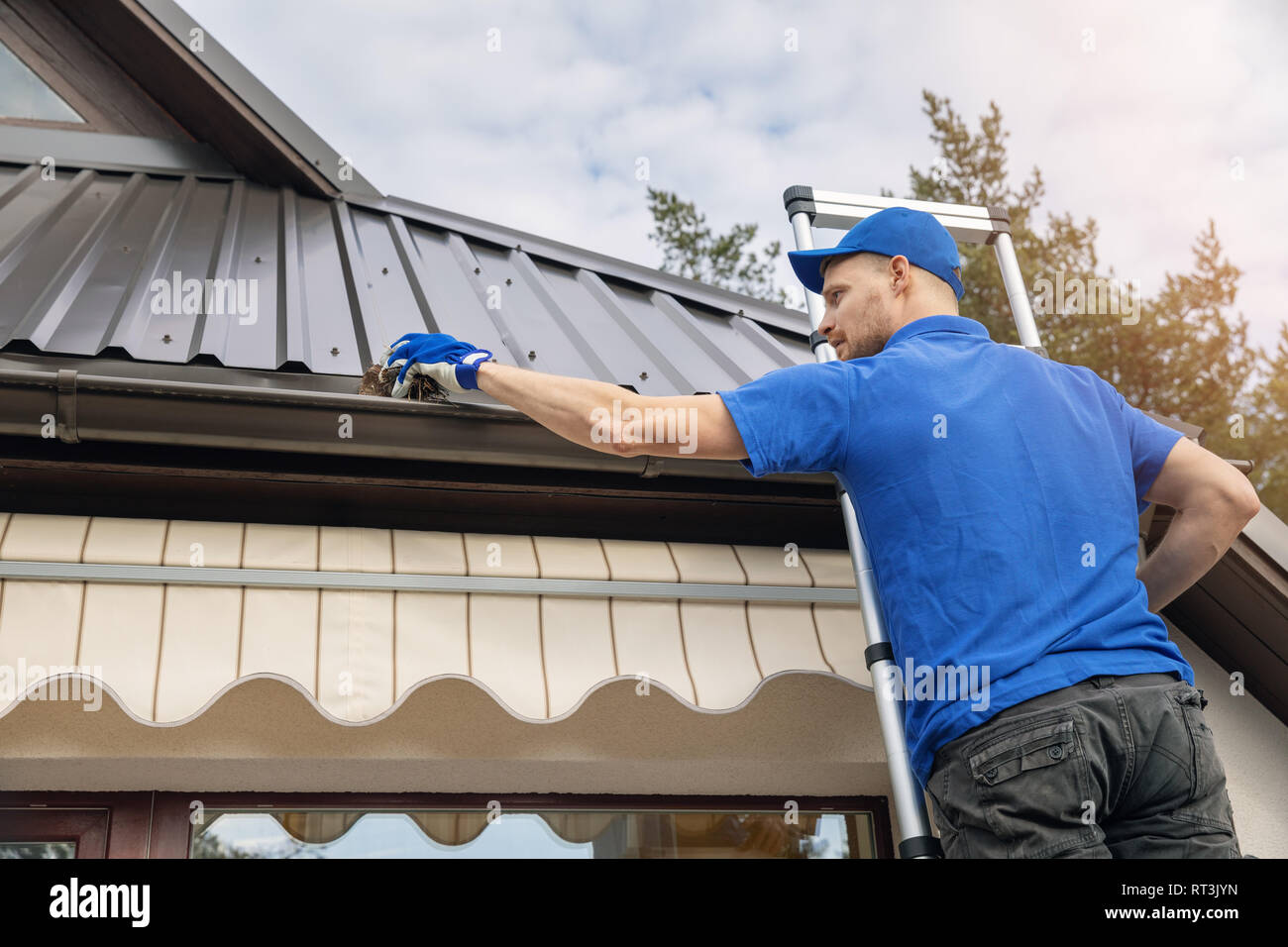 man standing on ladder and cleaning roof rain gutter from dirt Stock Photo