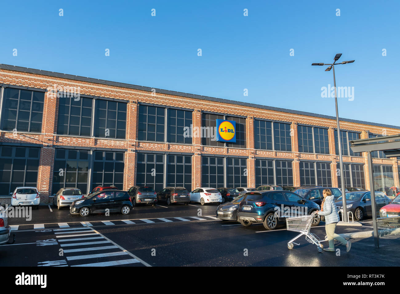 Tourcoing,FRANCE-February27,2019:Building, logo, cars in the parking lot and a woman with a shopping cart going shopping to the Lidl supermarket. Stock Photo