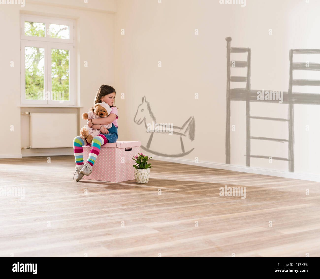 Girl in empty apartment sitting on a box holding teddy Stock Photo