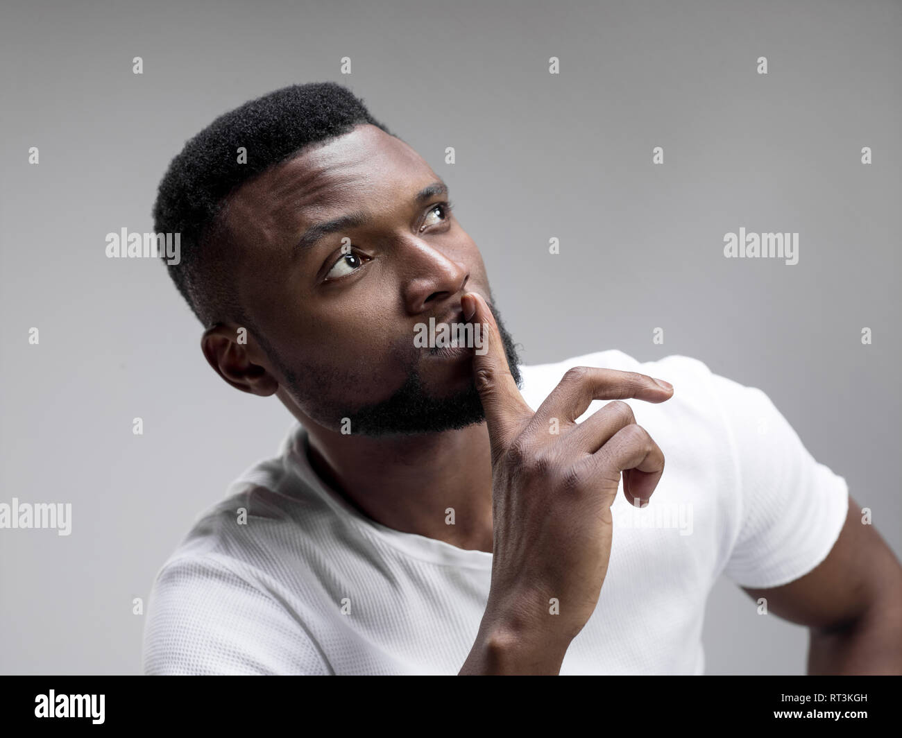 Serious african male keeps fore finger on lips, tries to keep conspiracy, says: Shh, make silence please. Isolated shot of man shows silence gesture Stock Photo