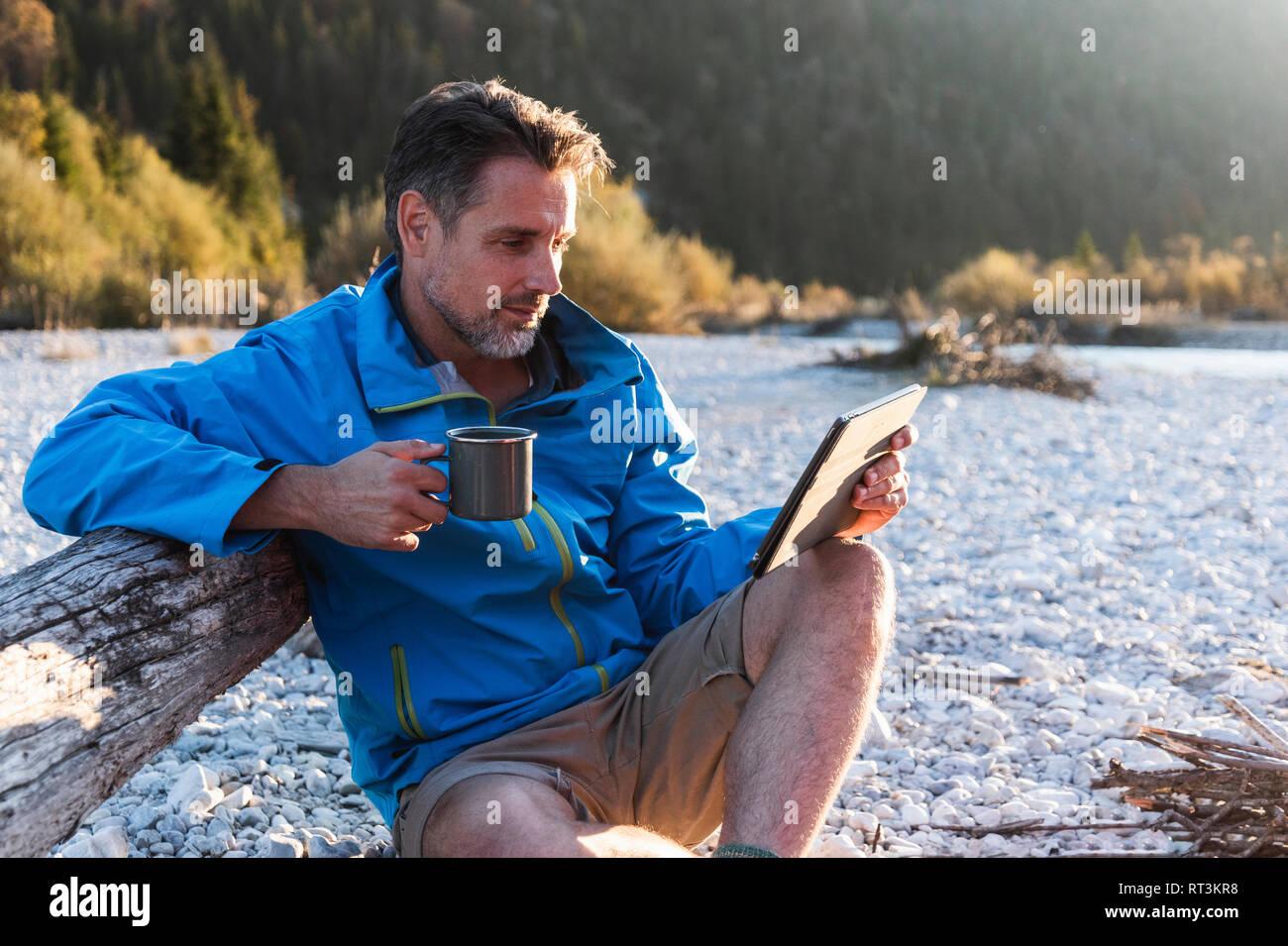 Mature man camping at riverside, using tablet Stock Photo