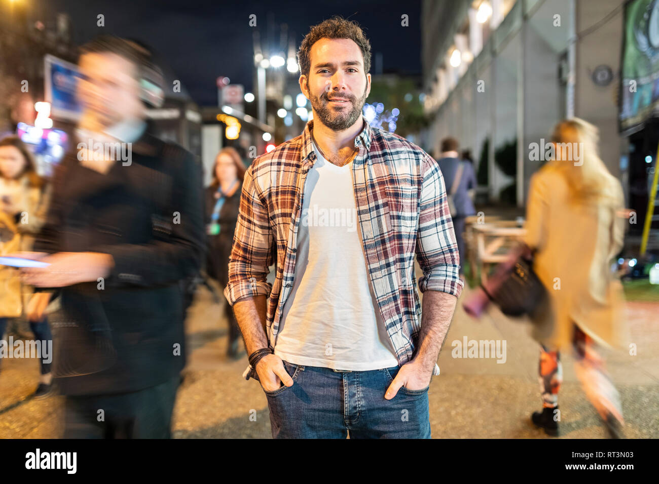 UK, London, portrait of a smiling commuter by night with blurred people passing nearby Stock Photo