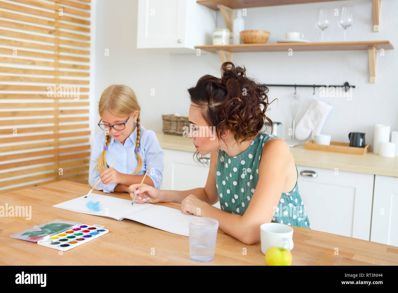 Mother and daughter painting together at home on the kitchen with ...