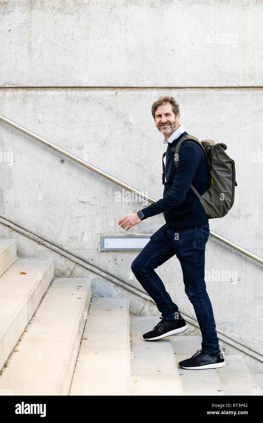 Smiling mature man with a backpack walking up stairs in the city Stock Photo