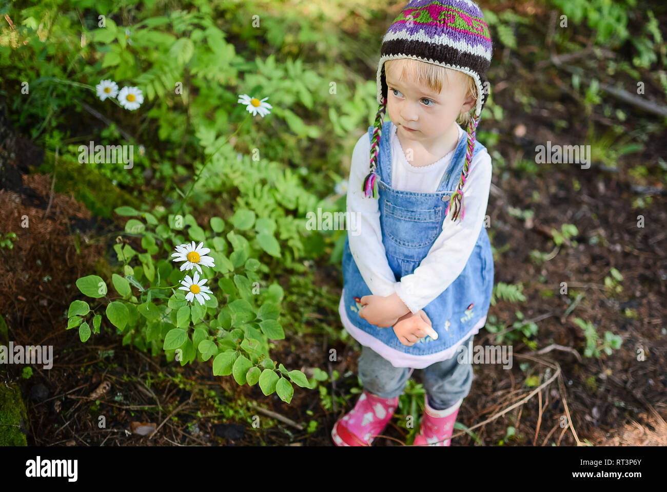 Portrait of sad little girl wearing knitted hat and denim dress outdoors Stock Photo