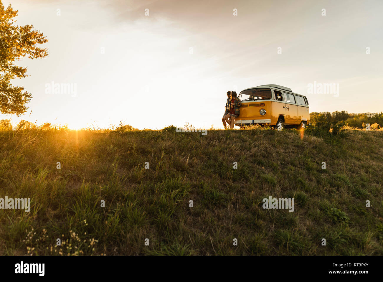 Young couple leaning on their camper, watching ghe sunset Stock Photo