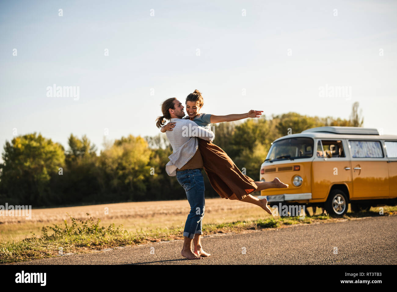 Happy couple doing a road trip with a camper, embracing on the road Stock Photo