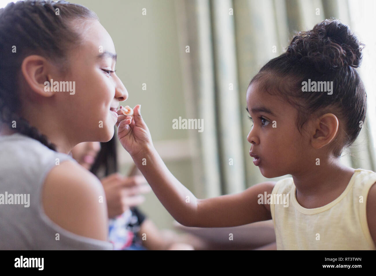 Cute toddler girl applying lip gloss to sister s lips Stock Photo