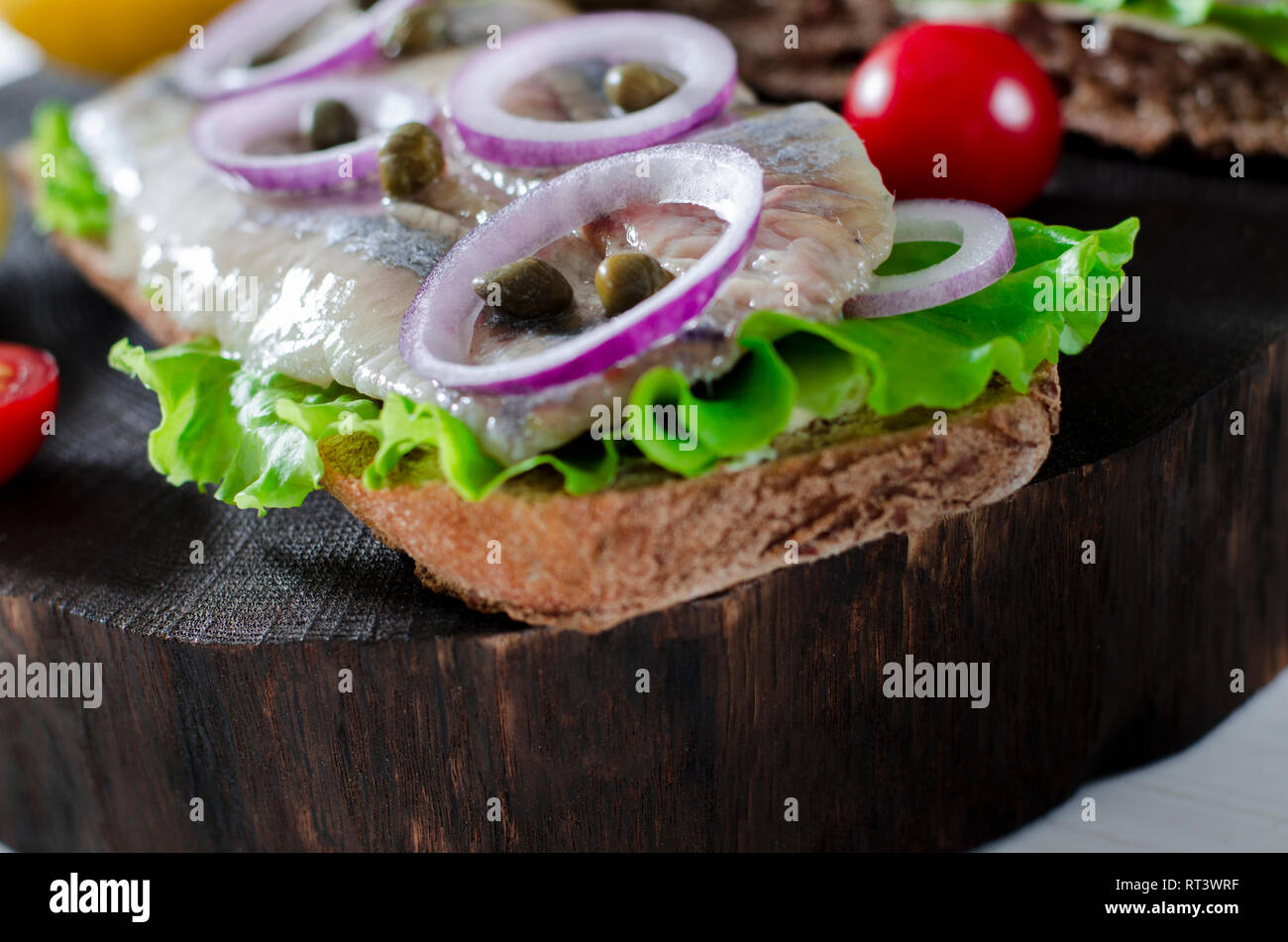 Herring fillet with salt, pepper, herbs, onion and lemon on black plate