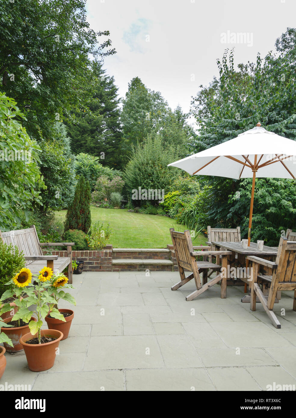 Garden in summer with patio, wooden garden furniture and a parasol or sun umbrella Stock Photo