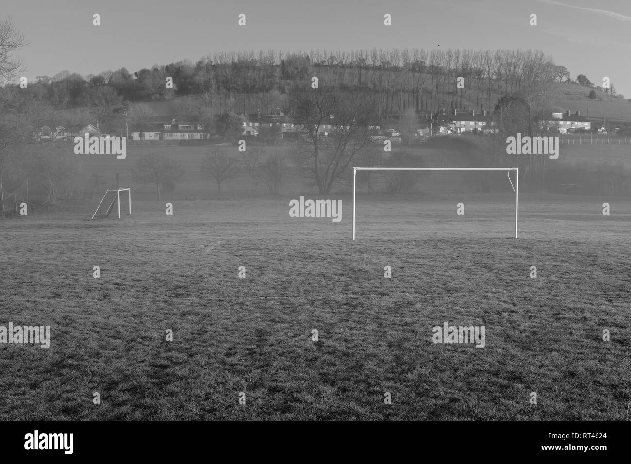 Empty village football field, small amount of fog drifting through, hill in the back ground with houses Stock Photo