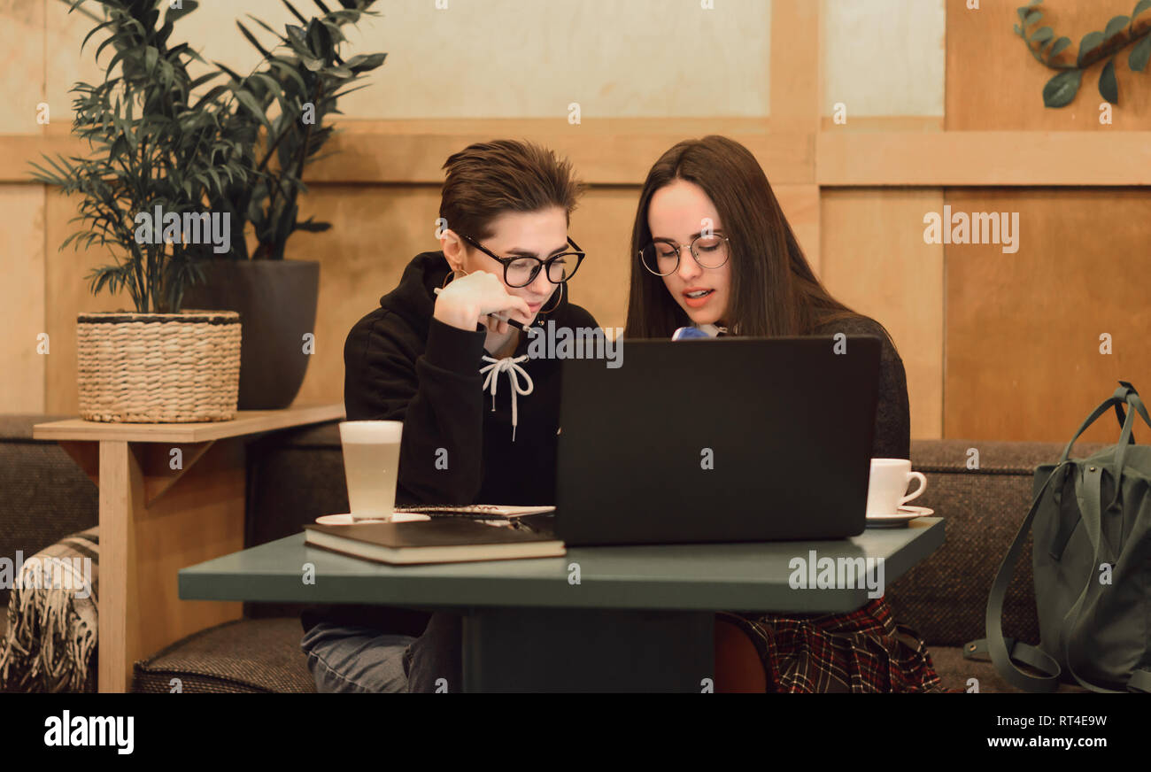 Pretty female students cooperating for completing common project learning in cafe interior with laptop computer Stock Photo