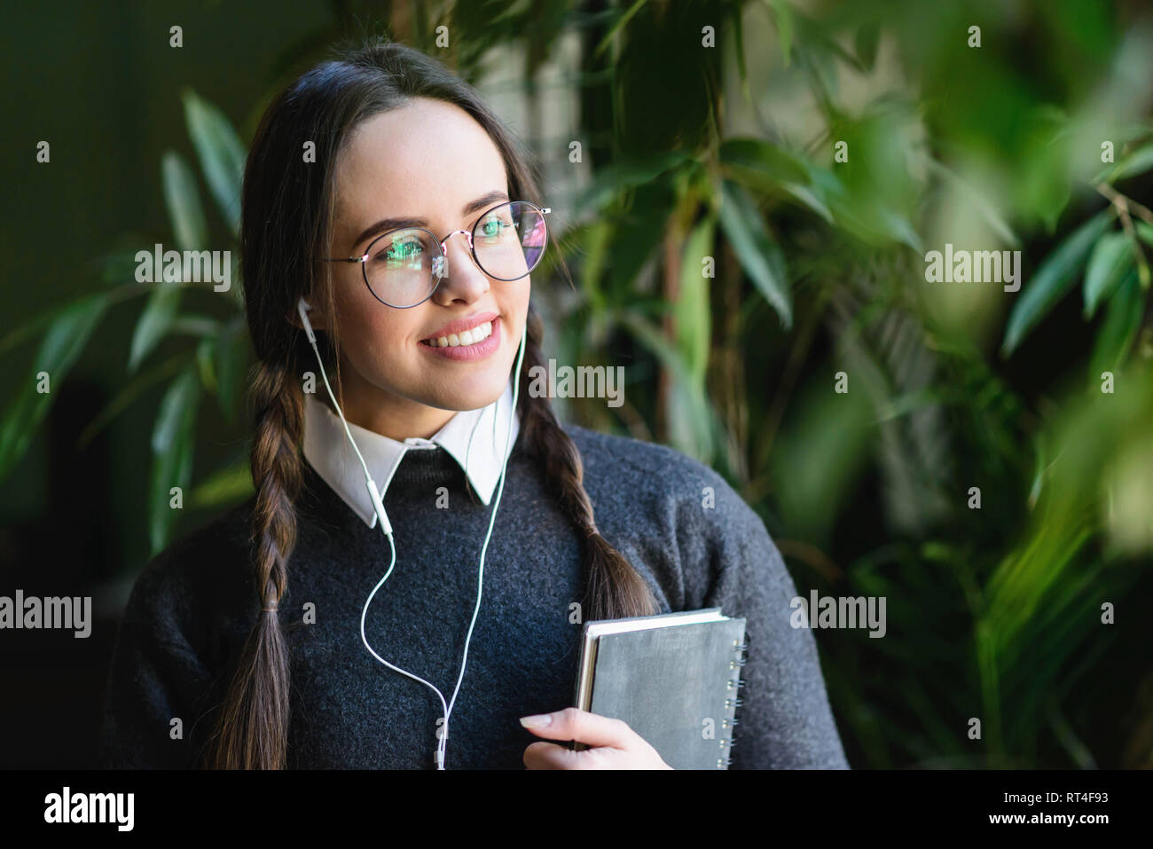 Brunette girl with braids wearing uniform standing near the window and listening music Stock Photo