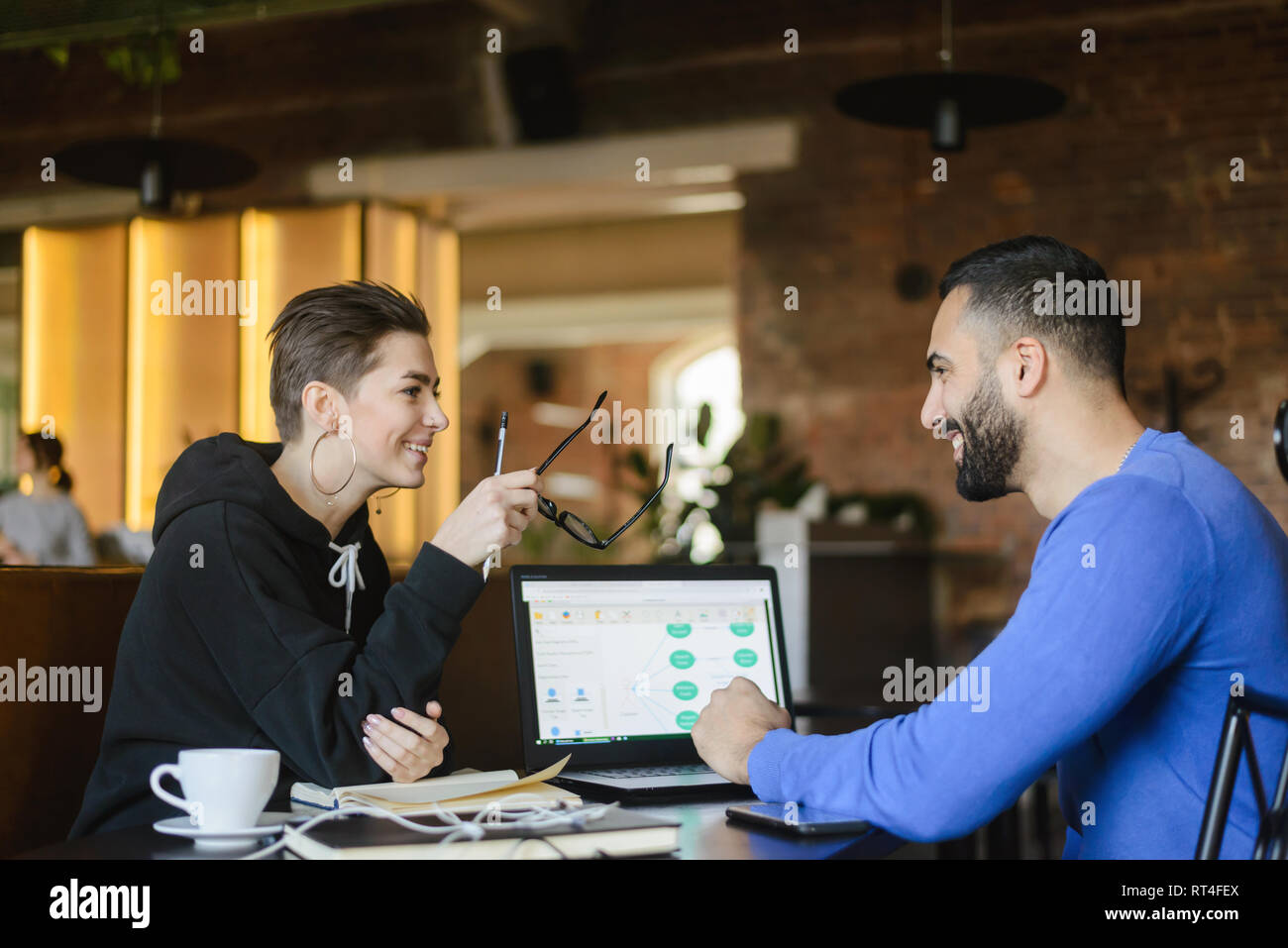 Positive male and female students cooperating using laptop computer for a learning sitting at the cafe Stock Photo