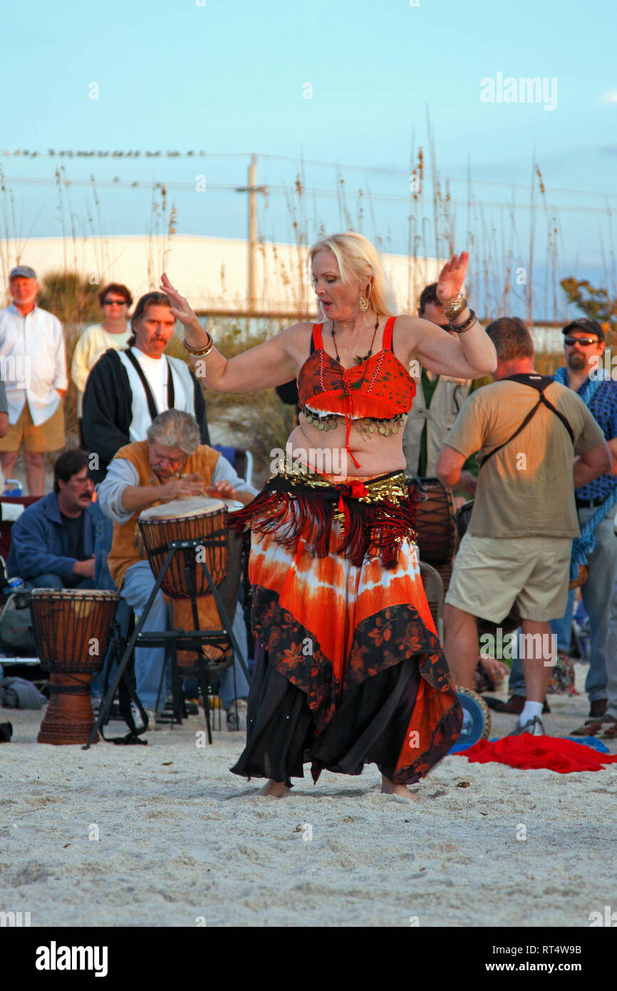 woman belly dancing, sand beach; drummers; sunset celebration; entertainment; music, fun, talent, Nokomis; FL; Florida; winter; vertical Stock Photo