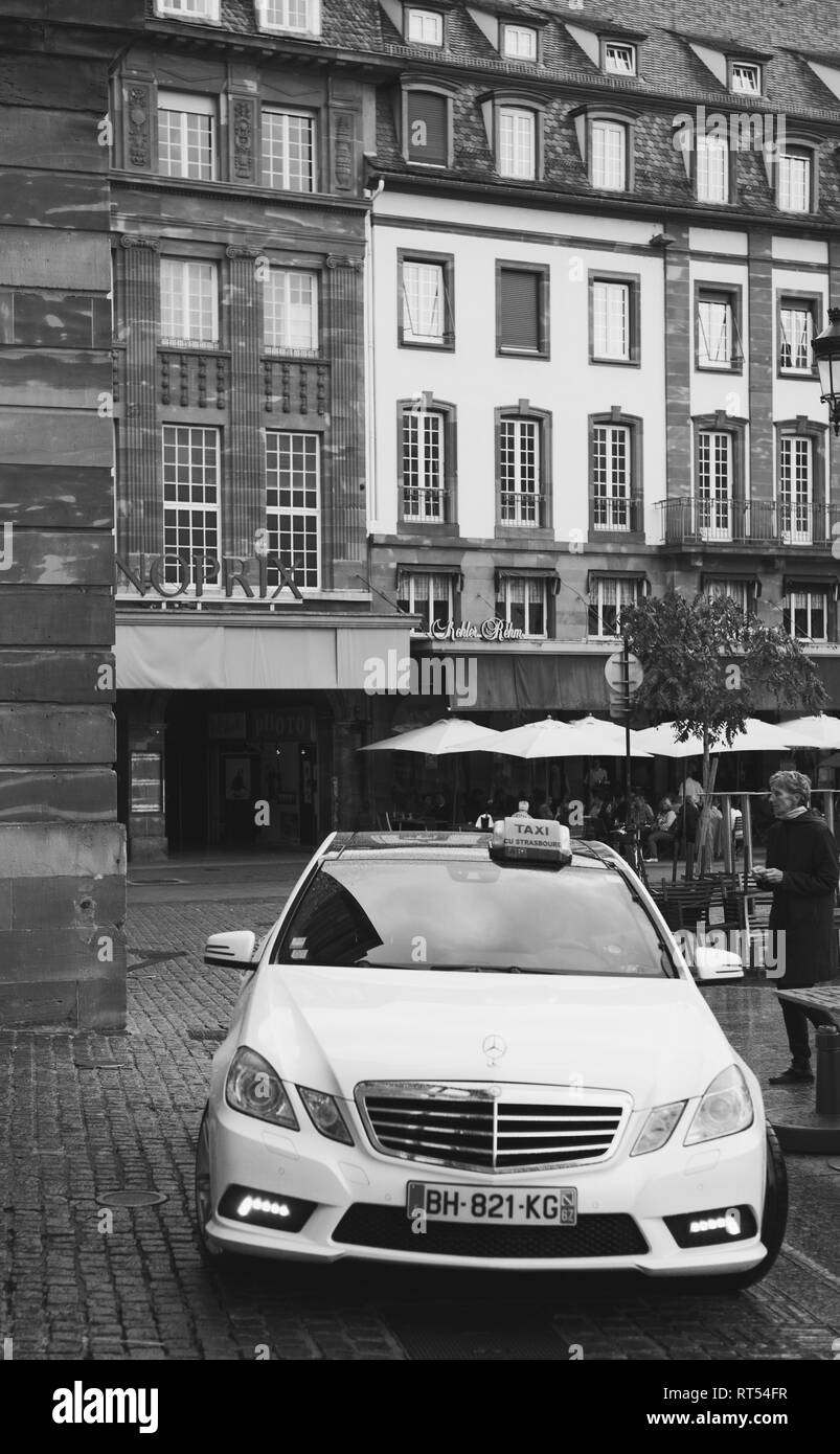 STRASBOURG, FRANCE - SEP 21, 2014: Black and white image of Mercedes-Benz E Class taxi parked on a rainy day in center of Strasbourg, place Kleber next to cafe Stock Photo