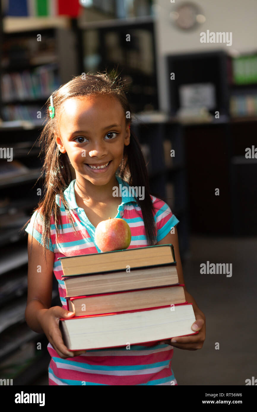 Schoolgirl holding stack of books and apple in the library Stock Photo ...