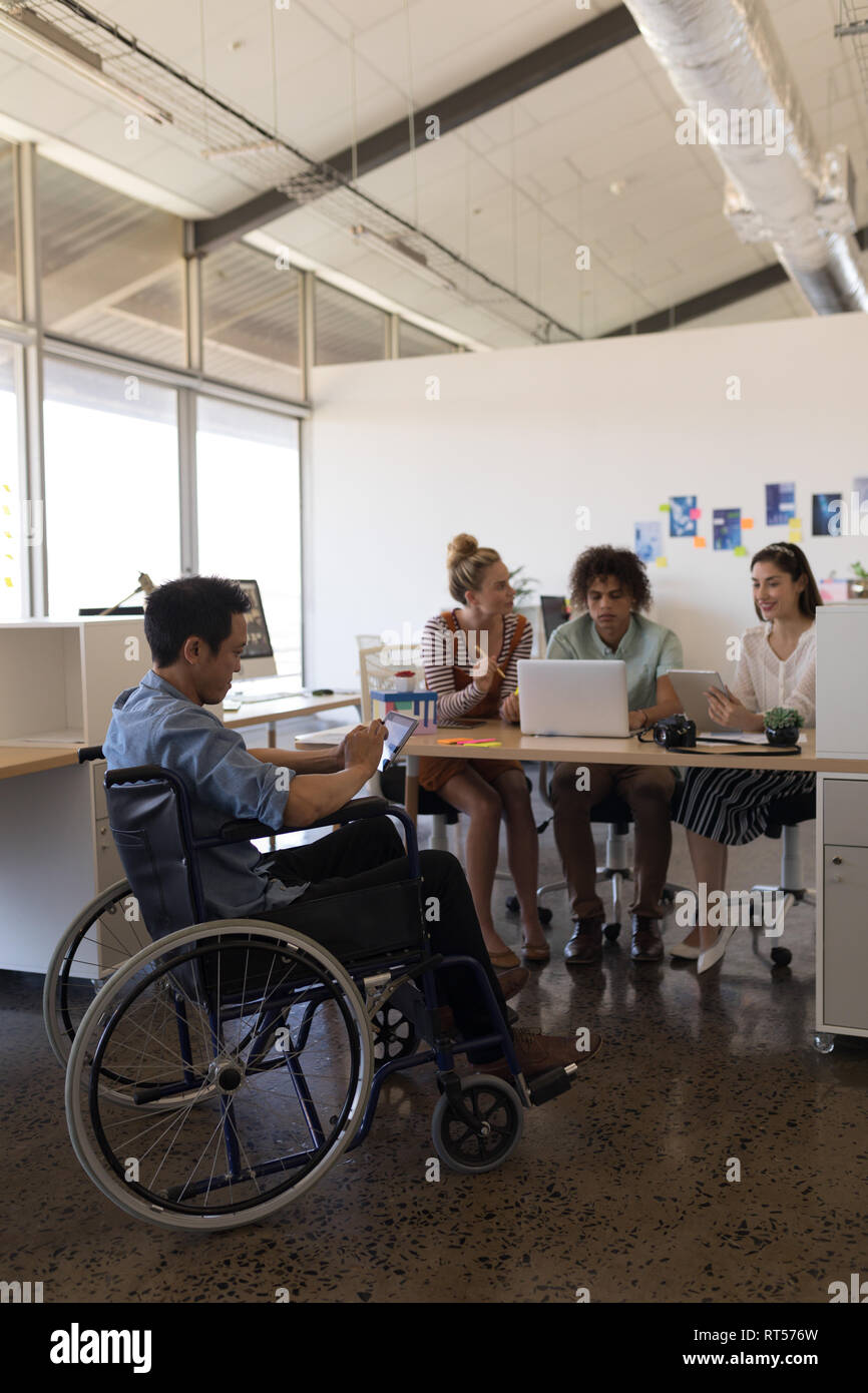 Disabled male executive using digital tablet while coworkers working in the background Stock Photo