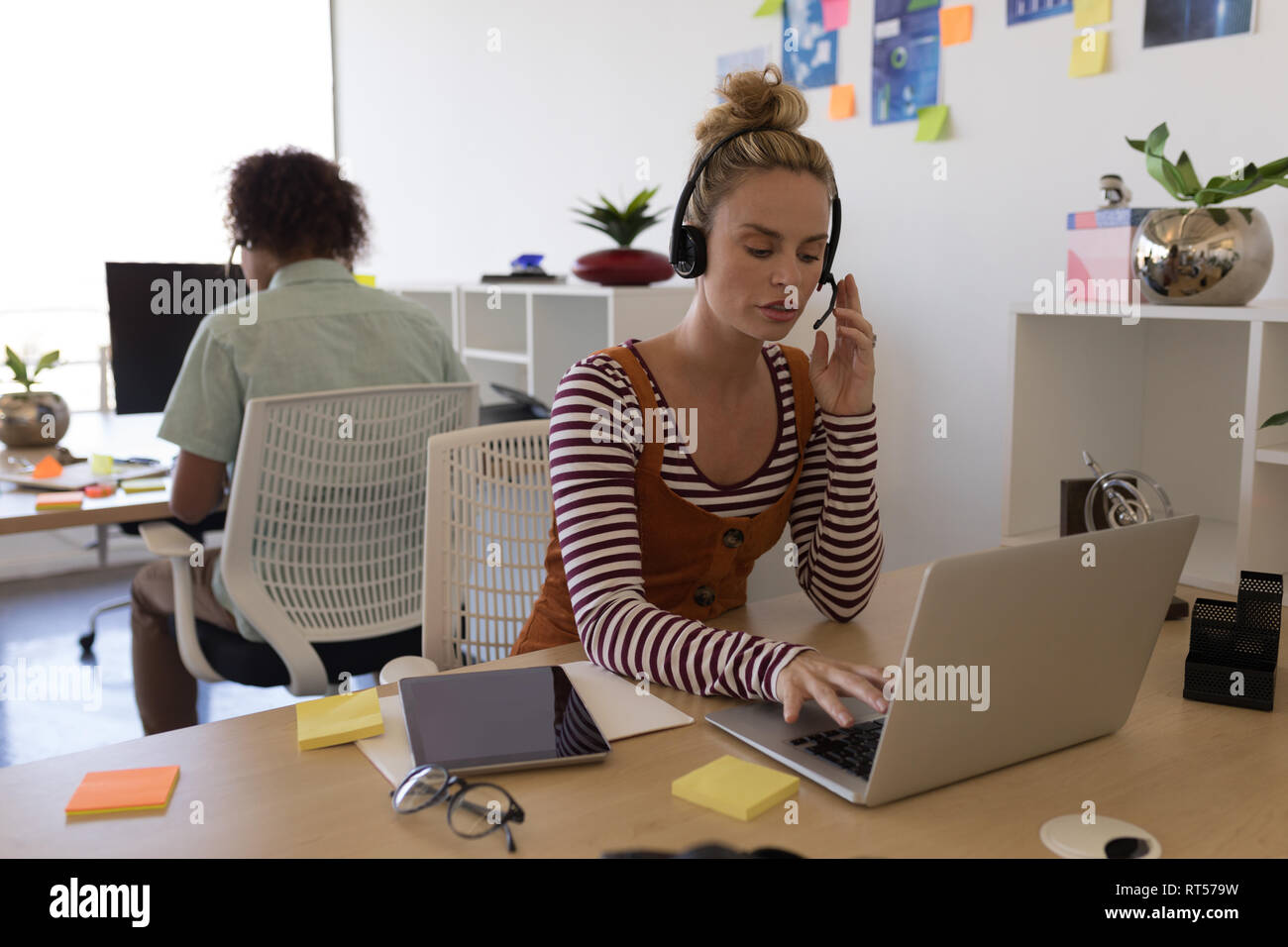 Female executive using laptop while taking on headset at desk Stock Photo
