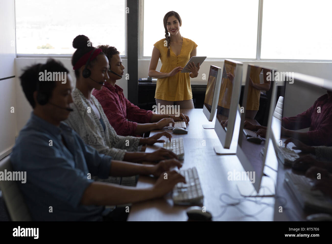 Female executive using digital tablet while coworkers talking on headset Stock Photo