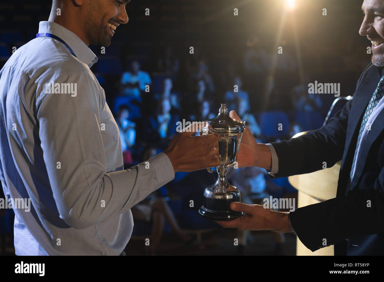 Businessman giving trophy to business male executive on stage in auditorium Stock Photo