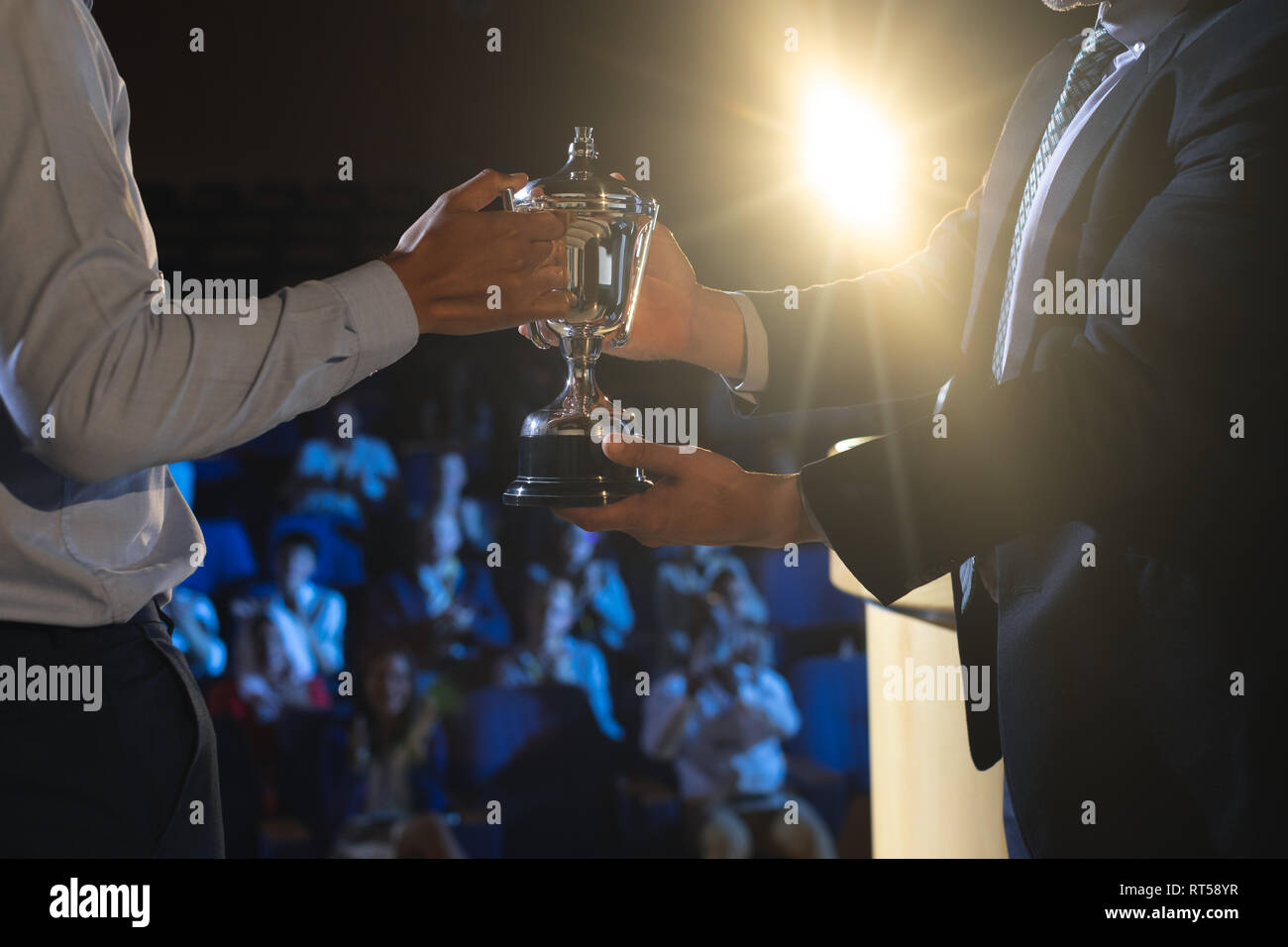 Businessman giving trophy to business male executive on stage in auditorium Stock Photo
