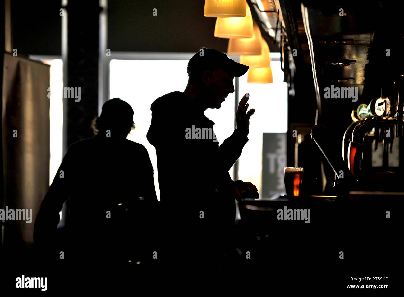 Silhouette of two men wearing baseball caps at bar in pub Stock Photo