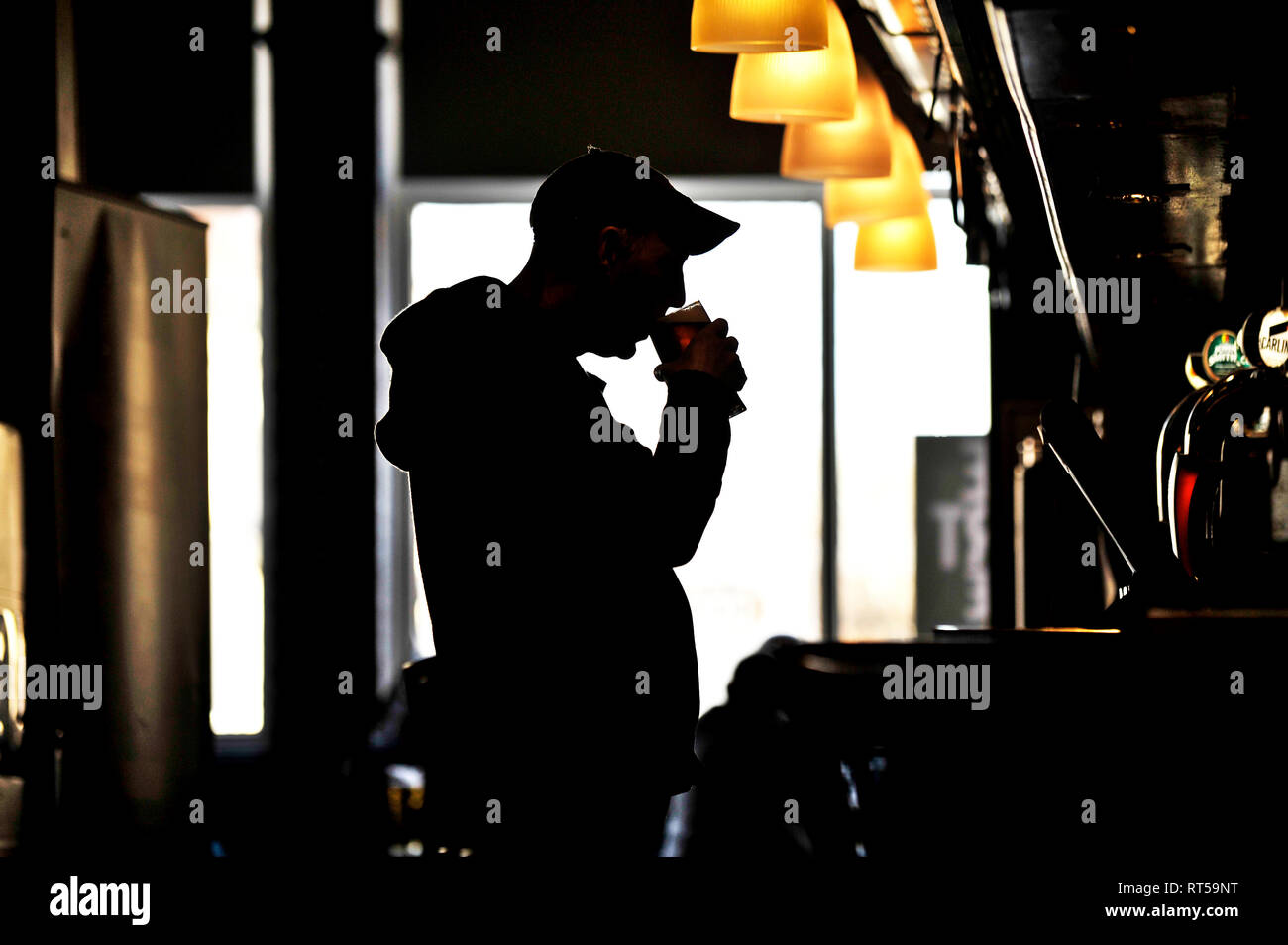 Silhouette of unidentified man wearing baseball cap drinking beer at bar in pub Stock Photo