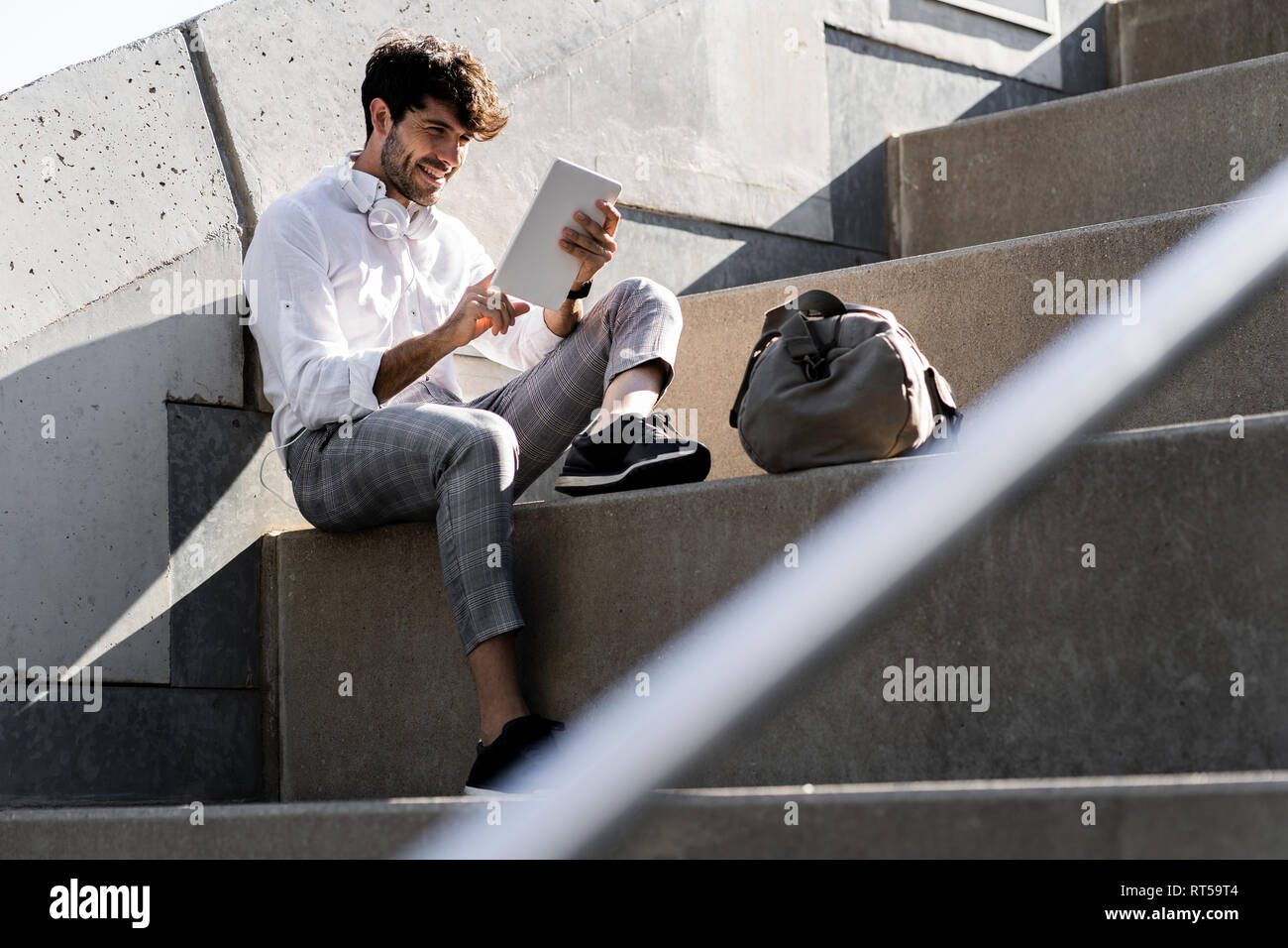 Smiling young man sitting on stairs outdoors using tablet Stock Photo ...