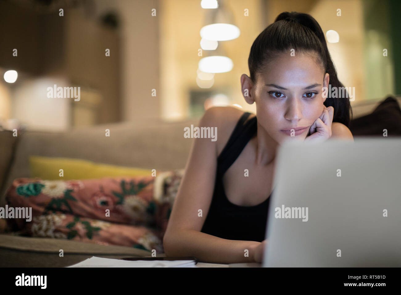 Focused woman in pajamas using laptop on sofa Stock Photo