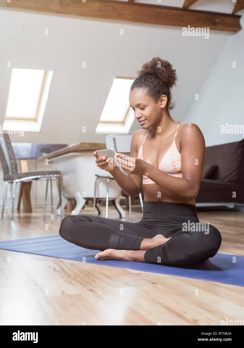 Young woman sitting on yoga mat using cell phone Stock Photo