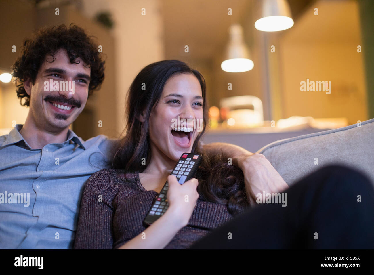 Laughing couple watching TV on sofa Stock Photo