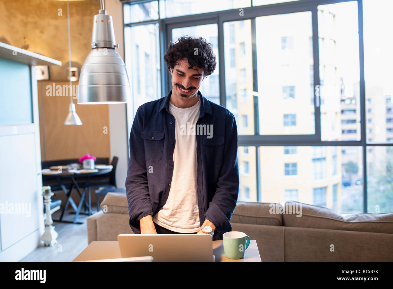 Smiling man using laptop in apartment Stock Photo