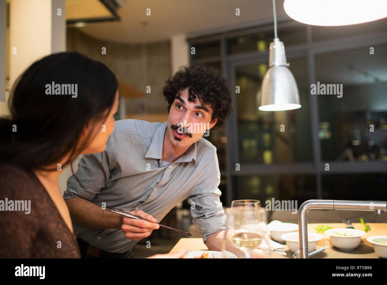 Couple eating dinner with chopsticks in apartment kitchen Stock Photo