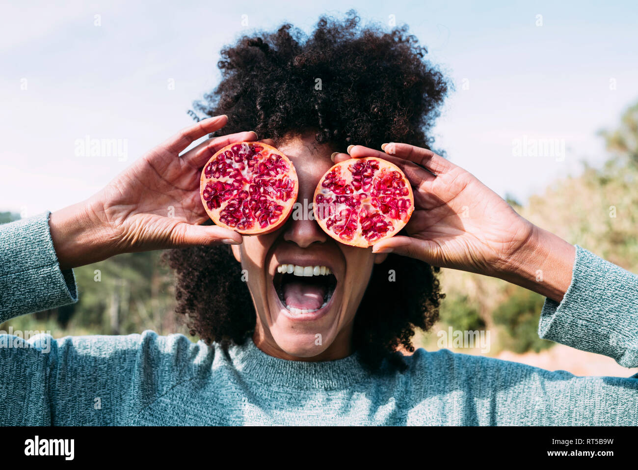 Woman standing in the countryside, covering eyes with halved pomegranates Stock Photo