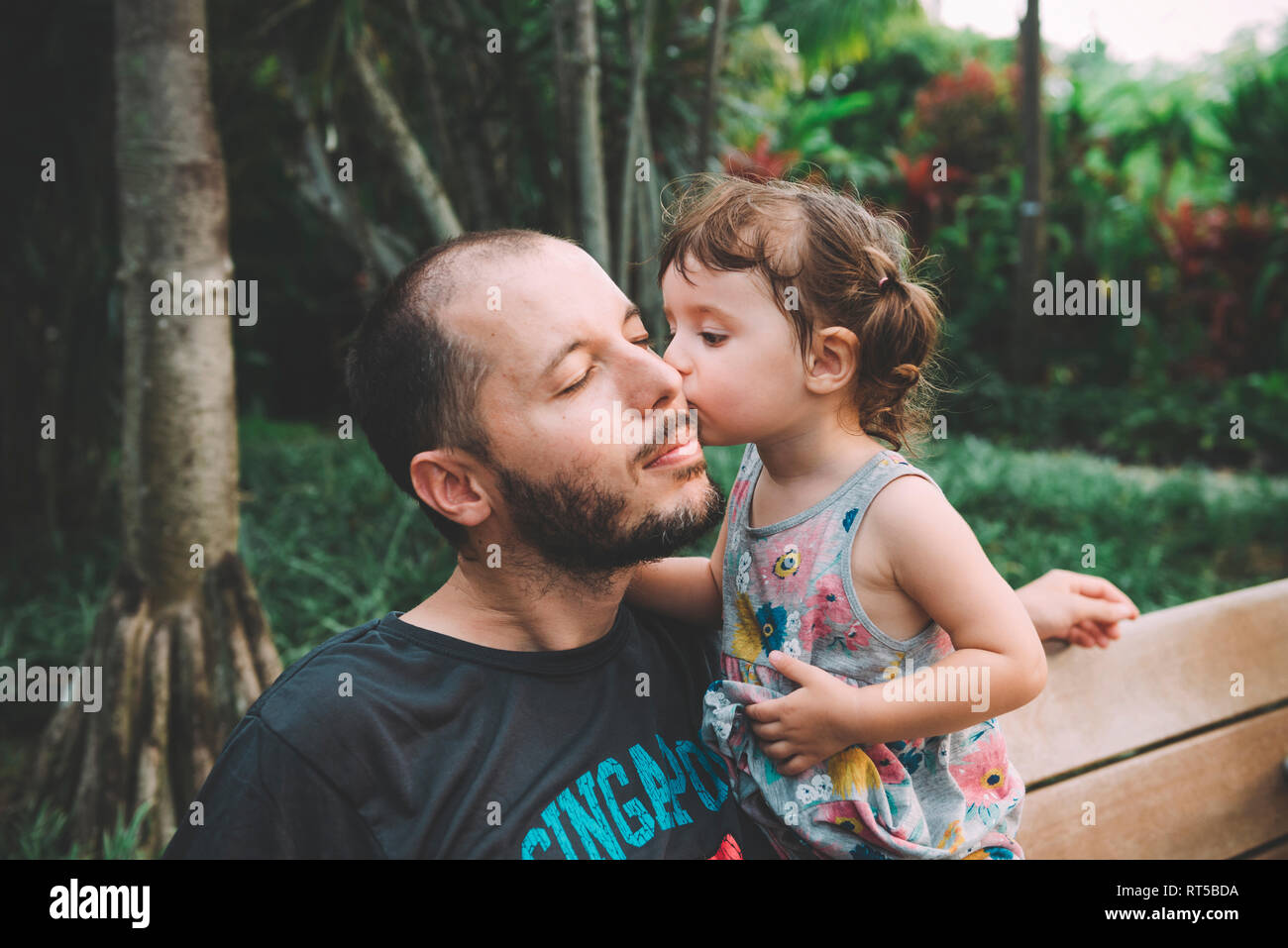 Baby girl kissing her father on cheek in a park Stock Photo