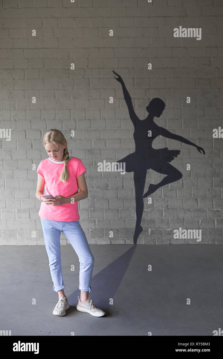 Blond girl with smartphone and shadow of ballerina in the background Stock Photo