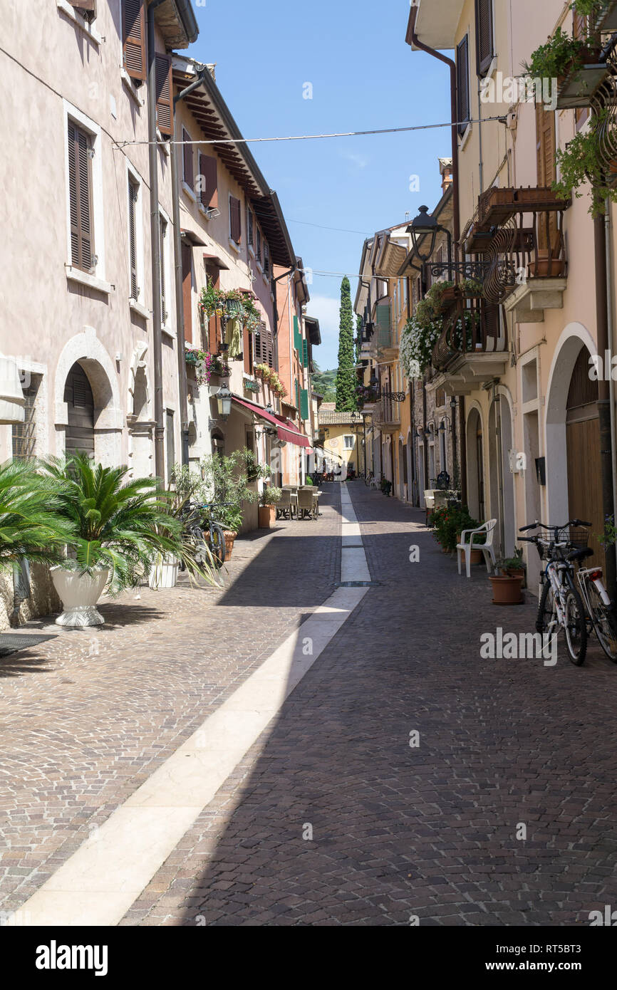 BARDOLINO, VENETO REGION, ITALY - AUGUST 7, 2017: narrow street with restaurants and shops with colorful facades of tenements and blue sky. Stock Photo