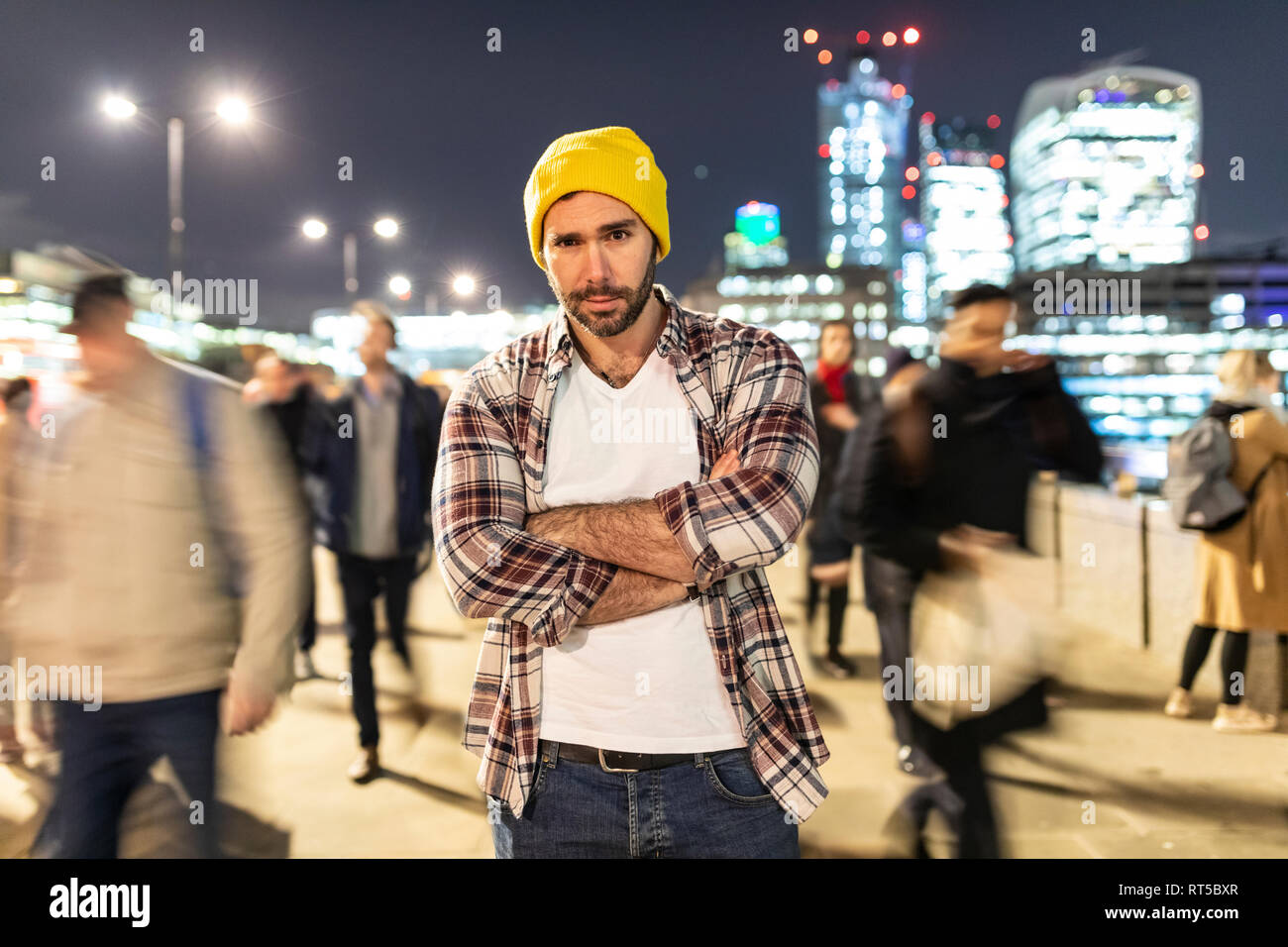 UK, London, portrait of a commuter by night with blurred people passing nearby Stock Photo