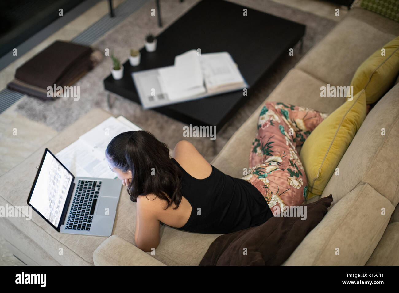 Woman in pajamas working at laptop on living room sofa Stock Photo